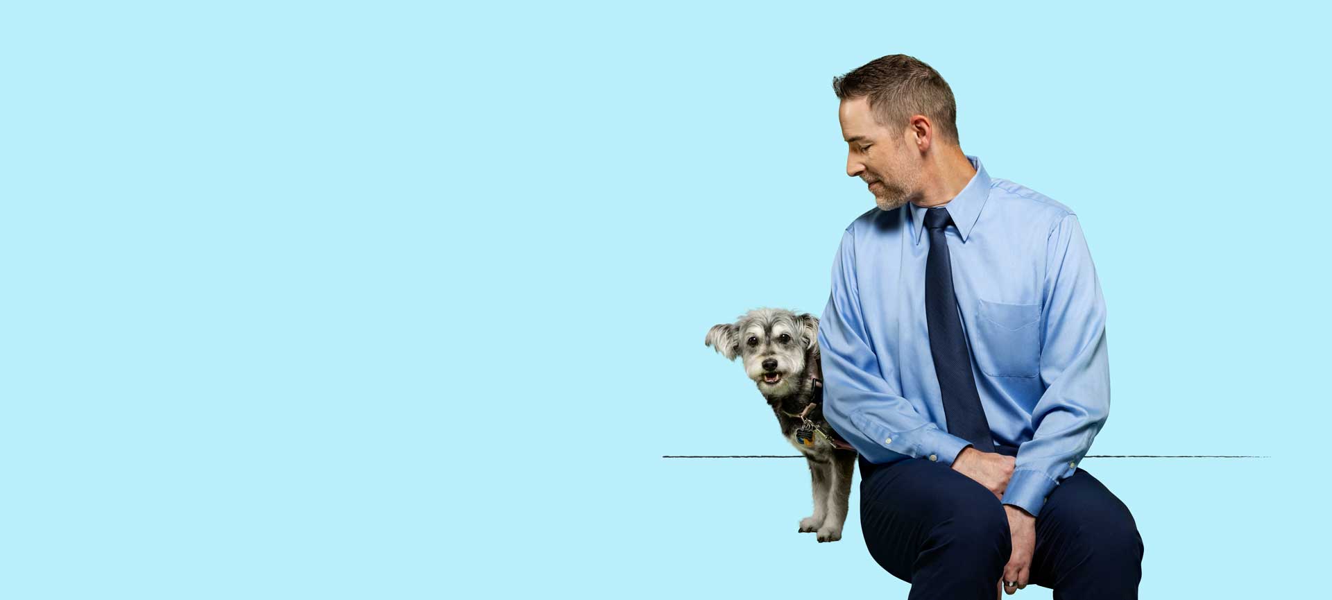 A man sitting down and smiling while looking at his older dog 