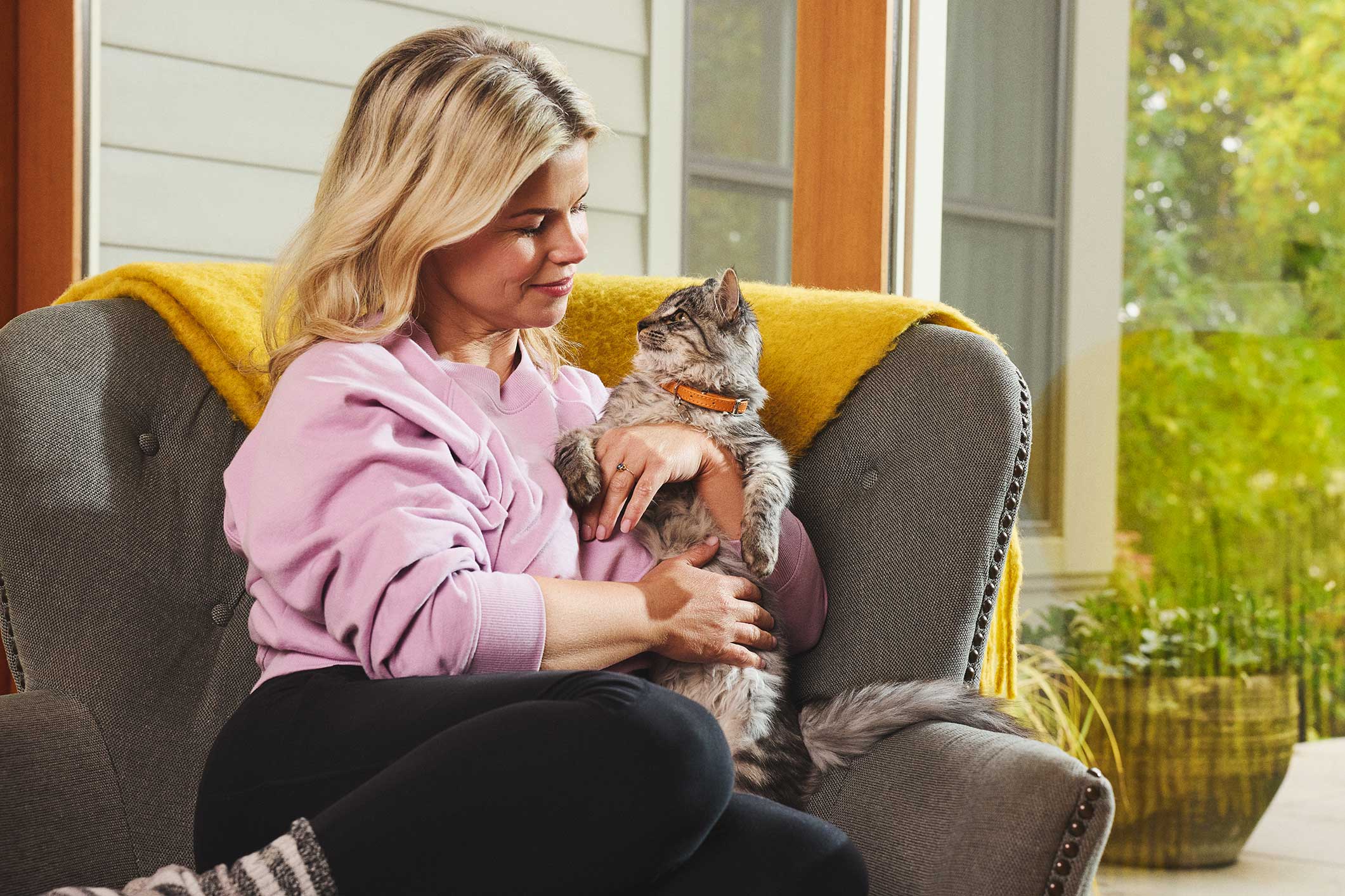 A woman holding her cat sits on a couch 