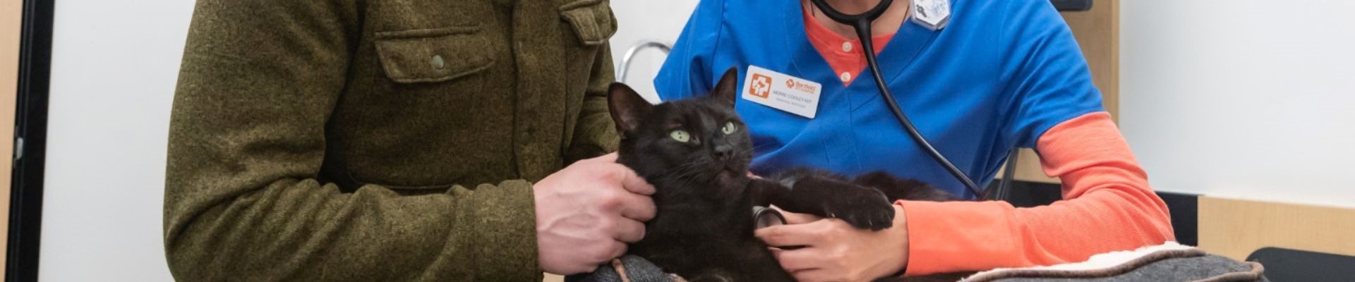 A Banfield veterinary professional sits next to a cat owner holding his black cat